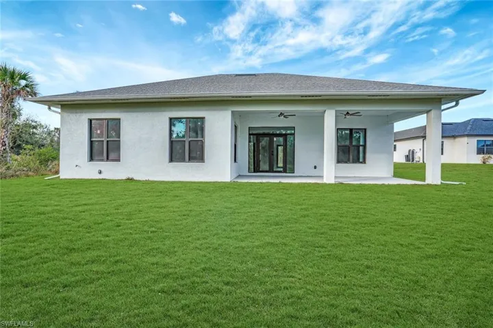 Rear view of property with ceiling fan, a patio area, and a lawn