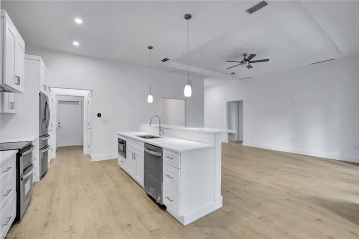 Kitchen with stainless steel appliances, white cabinetry, and an island with sink