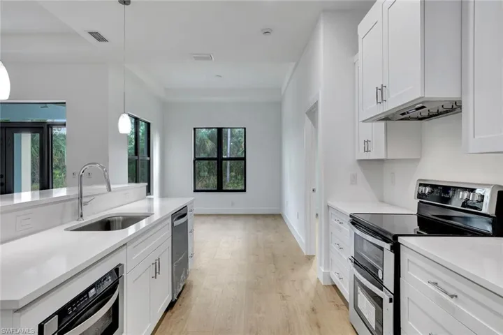 Kitchen featuring white cabinets, sink, stainless steel appliances, and hanging light fixtures