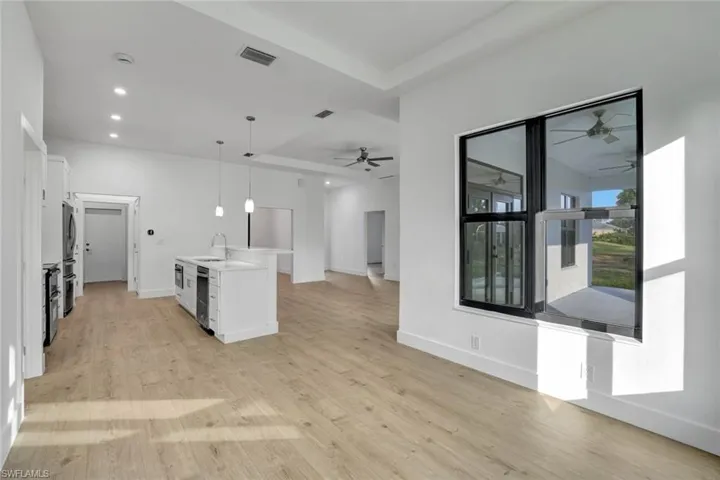 Kitchen featuring white cabinetry, sink, hanging light fixtures, a kitchen island with sink, and light wood-type flooring