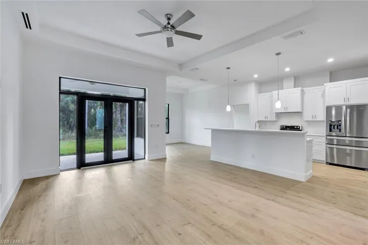 Kitchen featuring stainless steel refrigerator with ice dispenser, decorative light fixtures, a center island with sink, white cabinets, and light hardwood / wood-style floors