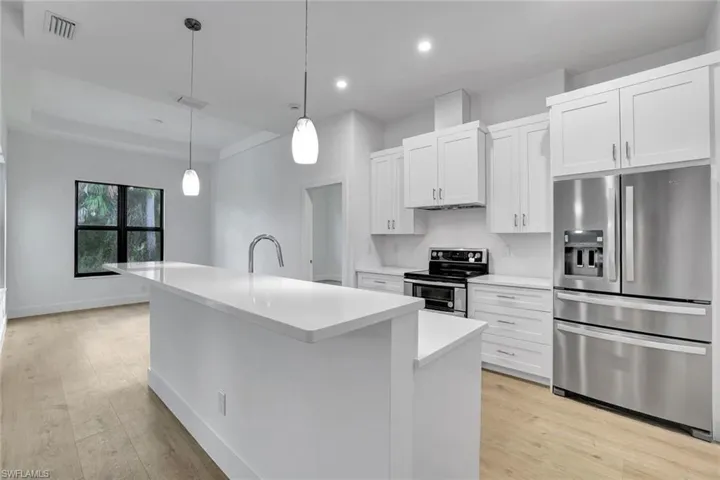 Kitchen featuring white cabinetry, pendant lighting, a center island with sink, appliances with stainless steel finishes, and light wood-type flooring