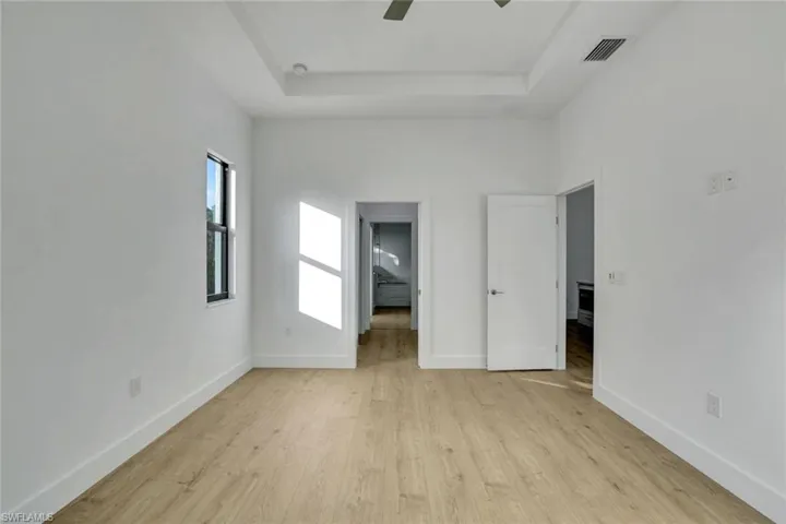 Unfurnished bedroom with light wood-type flooring, a tray ceiling, and ceiling fan