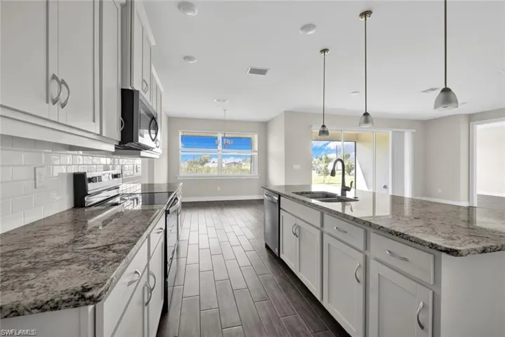 Kitchen featuring stainless steel appliances, white cabinetry, a kitchen island with sink, decorative light fixtures, and light stone countertops