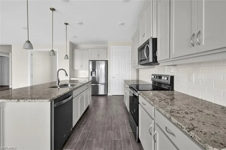 Kitchen with stainless steel appliances, light stone countertops, a center island with sink, decorative light fixtures, and wood tiled floors