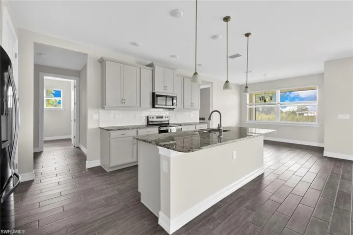 Kitchen with dark stone countertops, an island with sink, stainless steel appliances, tasteful backsplash, and decorative light fixtures