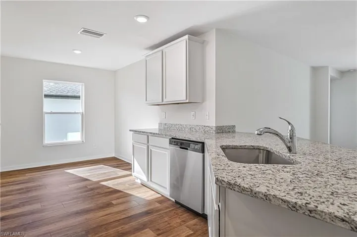 Kitchen featuring stainless steel dishwasher, wood-type flooring, light stone counters, sink, and white cabinetry