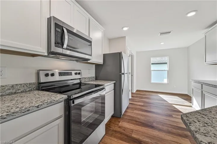 Kitchen featuring light stone countertops, dark hardwood / wood-style flooring, white cabinets, and appliances with stainless steel finishes