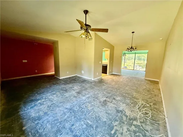 Carpeted empty room with lofted ceiling, baseboards, visible vents, and ceiling fan with notable chandelier