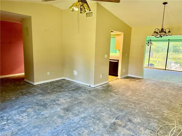 Empty room with baseboards, vaulted ceiling, visible vents, and ceiling fan with notable chandelier