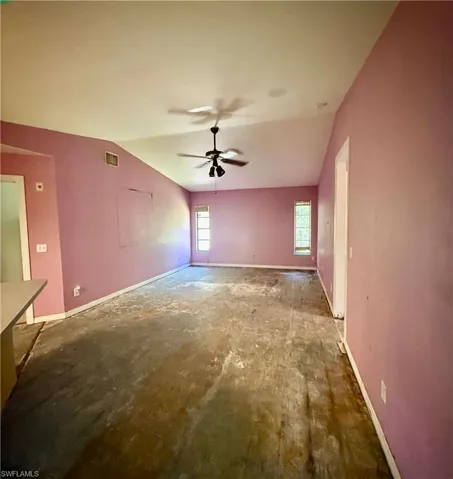 Unfurnished living room featuring vaulted ceiling, visible vents, baseboards, and ceiling fan