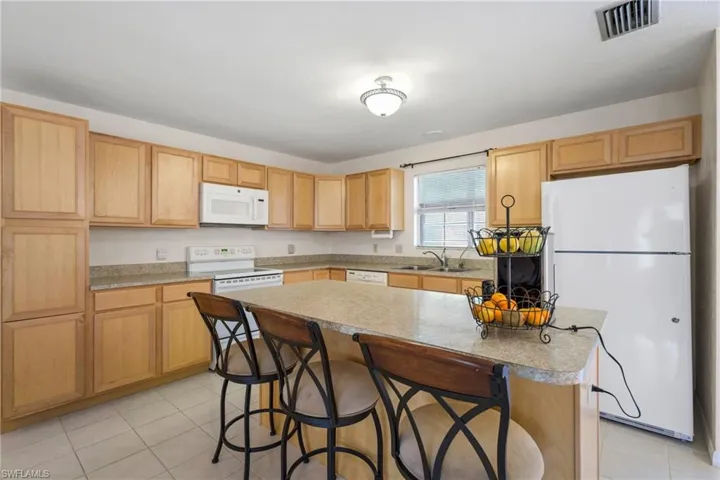 Kitchen with white appliances, light tile flooring, a center island, sink, and a kitchen bar