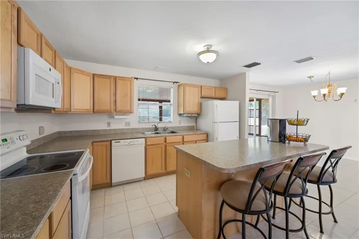 Kitchen with a kitchen breakfast bar, plenty of natural light, white appliances, and light tile flooring
