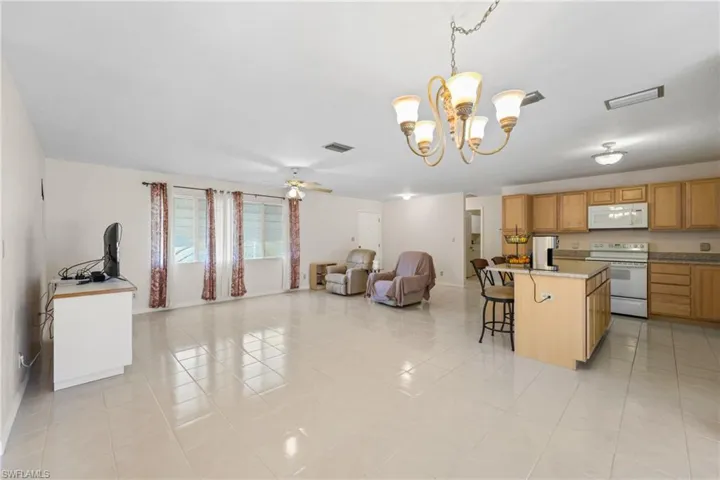 Kitchen featuring a kitchen breakfast bar, white appliances, pendant lighting, ceiling fan with notable chandelier, and light tile floors