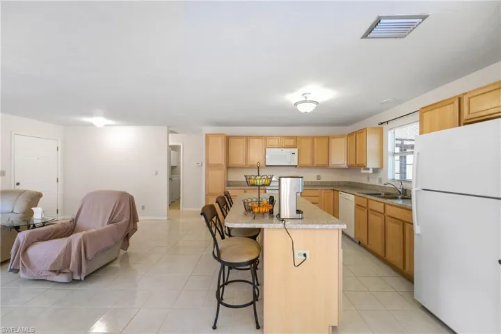 Kitchen with a kitchen island, a kitchen breakfast bar, sink, white appliances, and light tile floors