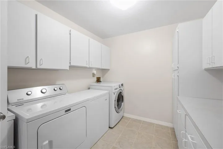 Clothes washing area with washer and dryer, washer hookup, cabinets, and light tile floors