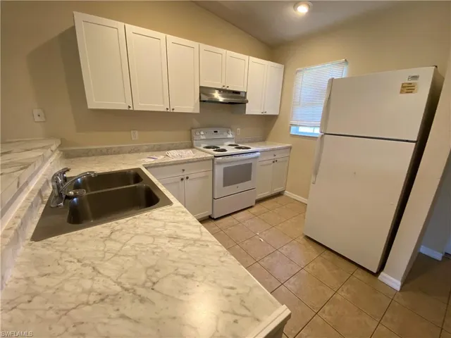 Kitchen featuring sink, white cabinets, vaulted ceiling, and white appliances.