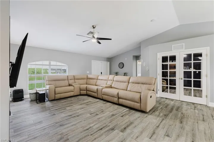 Living area featuring vaulted ceiling, light wood-style floors, ceiling fan, and french doors