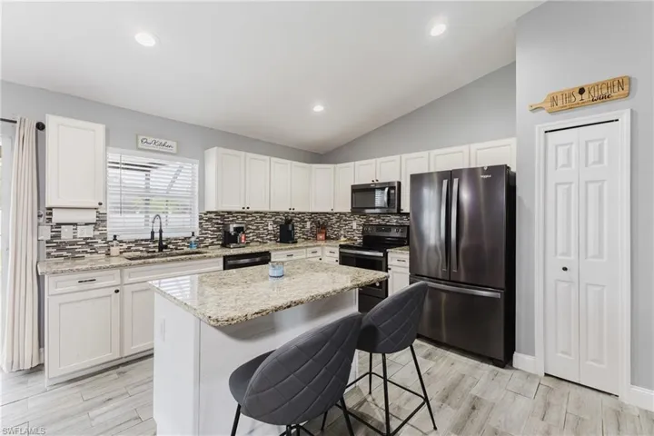 Kitchen featuring stainless steel appliances, a kitchen bar, light stone countertops, white cabinets, and vaulted ceiling