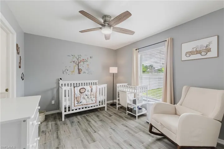 Bedroom with a crib, a ceiling fan, and wood tiled floors
