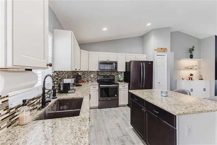 Kitchen featuring appliances with stainless steel finishes, vaulted ceiling, white cabinetry, a kitchen island, and light stone counters