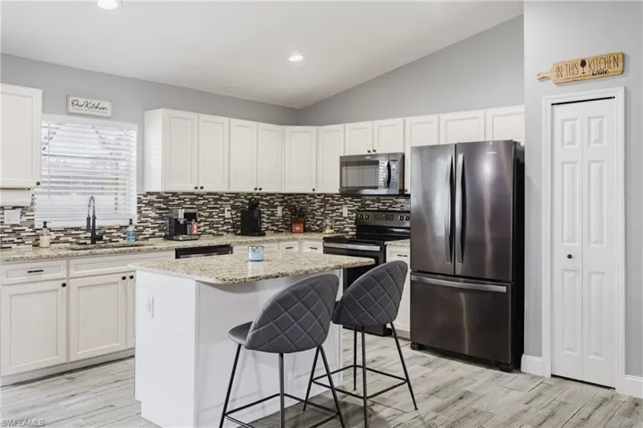 Kitchen with freestanding refrigerator, a breakfast bar, vaulted ceiling, white cabinets, and light stone countertops