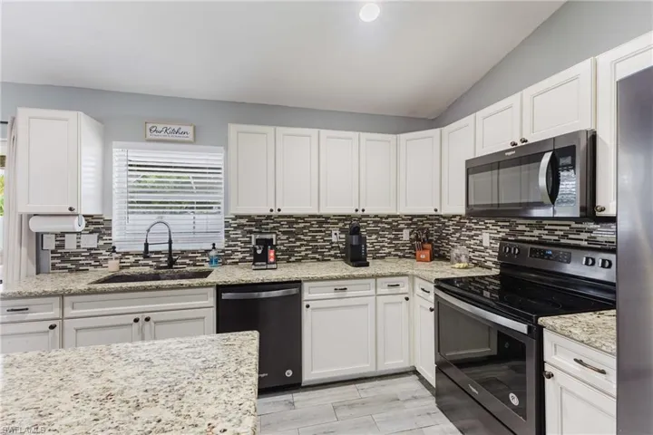 Kitchen with appliances with stainless steel finishes, white cabinetry, lofted ceiling, and light stone countertops
