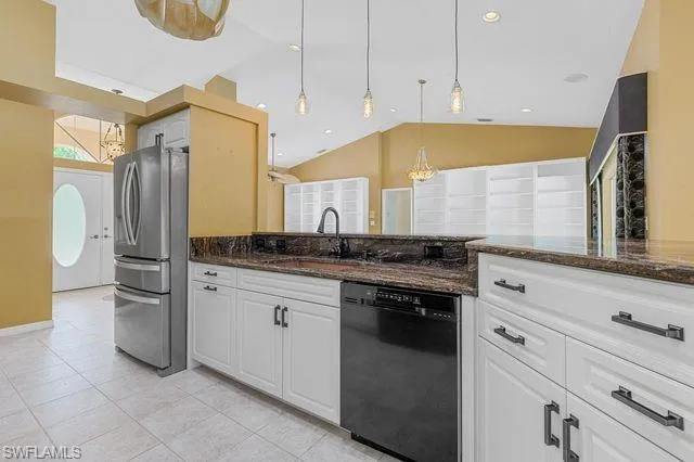 Kitchen with stainless steel fridge, dark stone countertops, dishwasher, and hanging light fixtures