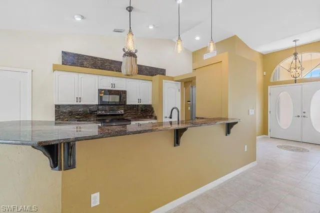 Kitchen featuring dark stone counters, white cabinets, electric stove, and pendant lighting