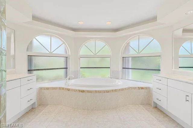 Bathroom with tile patterned flooring, tiled tub, a raised ceiling, and vanity