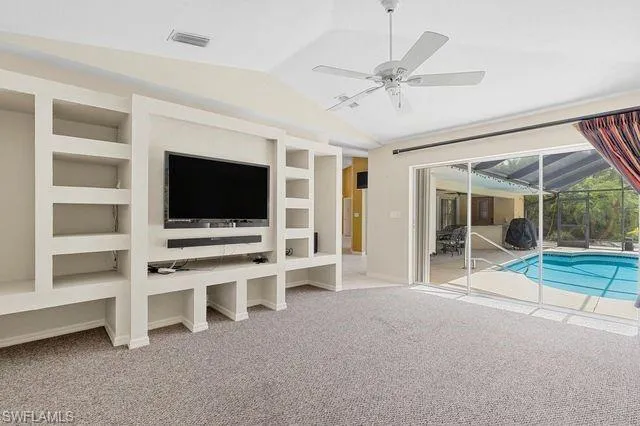 Unfurnished living room featuring built in features, carpet flooring, ceiling fan, and vaulted ceiling