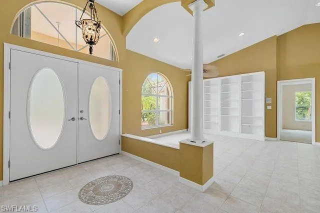 Tiled foyer with high vaulted ceiling, french doors, decorative columns, and plenty of natural light
