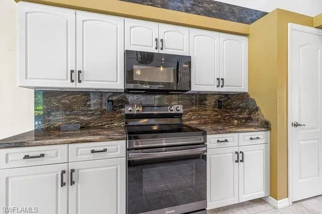 Kitchen with dark stone counters, stainless steel electric stove, white cabinets, and backsplash