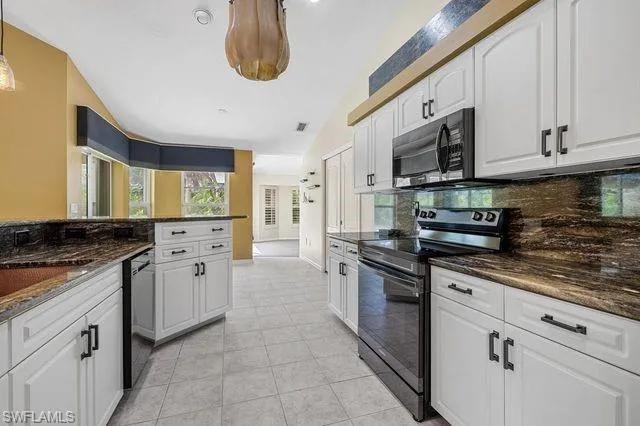 Kitchen with dark stone counters, light tile patterned flooring, black appliances, white cabinetry, and tasteful backsplash