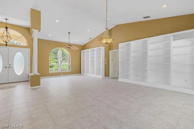 Unfurnished living room with light tile patterned flooring, a chandelier, built in shelves, high vaulted ceiling, and french doors