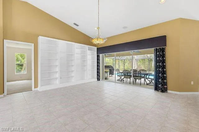 Empty room with light tile patterned flooring, a notable chandelier, built in features, and high vaulted ceiling