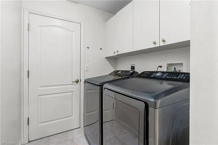 Laundry area featuring cabinets, light tile patterned floors, and washing machine and clothes dryer