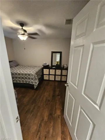 Bedroom with dark wood-type flooring, a textured ceiling, and a ceiling fan