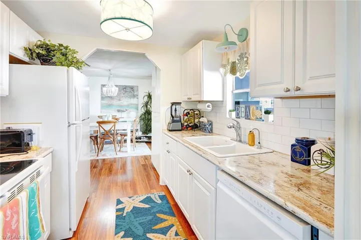 Kitchen with light wood finished floors, white appliances, tasteful backsplash, and an inviting chandelier