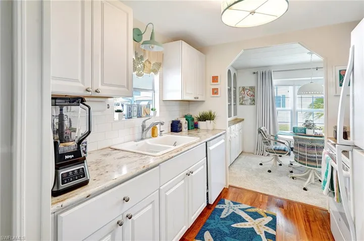 Kitchen with a sink, tasteful backsplash, wood finished floors, white appliances, and white cabinets