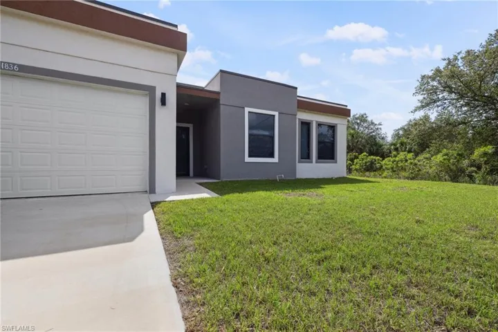 View of front of home with driveway, a front lawn, stucco siding, and an attached garage