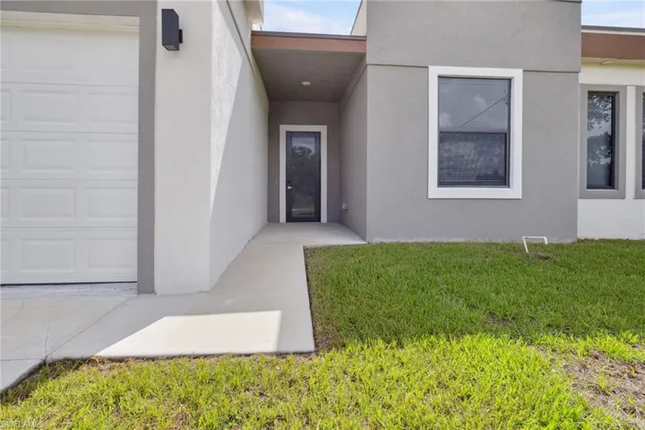 View of exterior entry featuring a garage, stucco siding, a yard, and concrete driveway