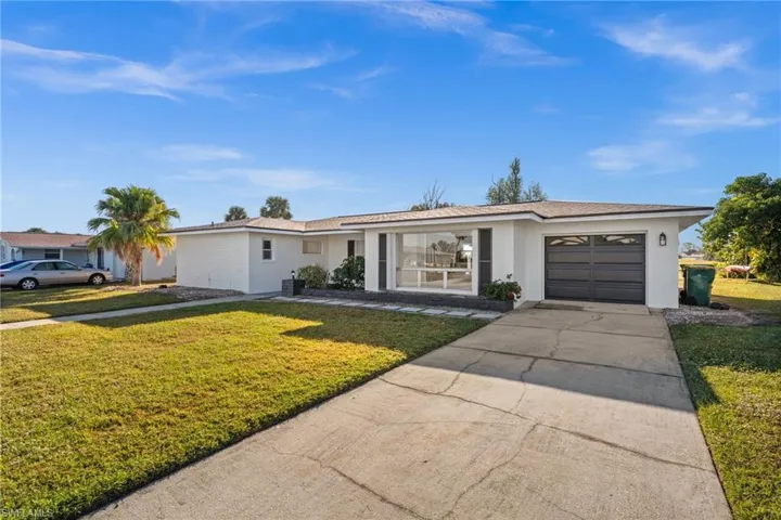 Ranch-style home with an attached garage, driveway, a front yard, and stucco siding