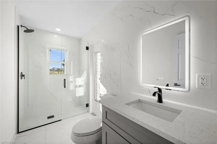 Bathroom with light marble finish floors, vanity, stone wall, a marble finish shower, and recessed lighting