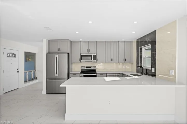 Kitchen featuring stainless steel appliances, gray cabinets, a peninsula, tasteful backsplash, and light marble finish flooring