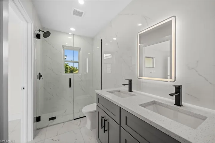 Full bathroom with light marble finish flooring, double vanity, a marble finish shower, recessed lighting, and stone wall