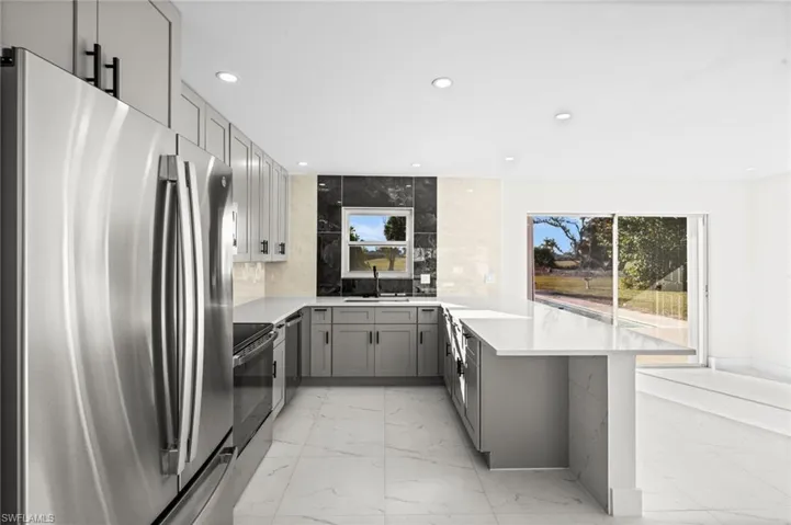 Kitchen with stainless steel appliances, gray cabinets, light marble finish floors, a peninsula, and recessed lighting