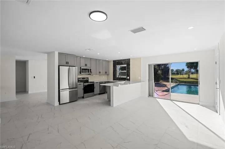 Kitchen with gray cabinets, light marble finish flooring, stainless steel appliances, backsplash, and a peninsula