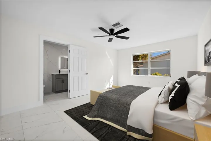 Bedroom with light marble finish floors, ensuite bath, and ceiling fan