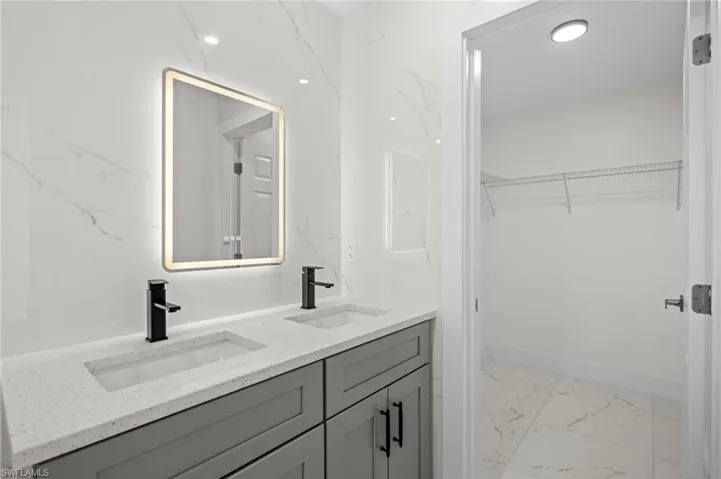 Bathroom featuring light marble finish floors, double vanity, a spacious closet, and recessed lighting